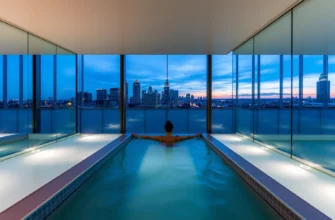 A serene scene of a modern cold plunge pool in a sleek spa setting, with a person standing in the water, surrounded by glass walls reflecting the Atlanta skyline at dusk, subtle lighting, no text or signage