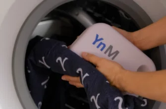 A photorealistic scene of a person gently washing a YnM weighted blanket in a washing machine, with water droplets and soft lighting, showing the blanket's texture and the machine's interior, no text or logos visible