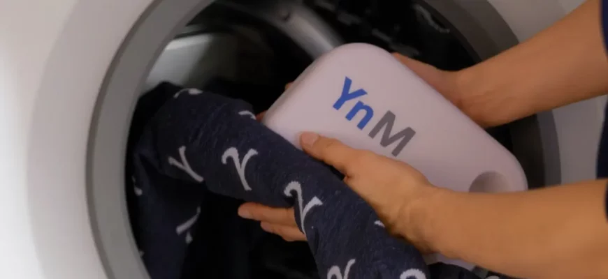 A photorealistic scene of a person gently washing a YnM weighted blanket in a washing machine, with water droplets and soft lighting, showing the blanket's texture and the machine's interior, no text or logos visible