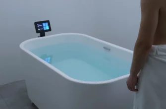 A sleek, modern cold plunge tub filled with crystal-clear water, set in a minimalist spa setting. A person in a towel stands beside the tub, looking at a digital display comparing top cold plunge models. The scene is bathed in cool blue lighting, with subtle reflections on the water surface.