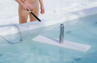 A clear, modern cold plunge pool with a sleek, stainless steel cleaning device in use, surrounded by a calm, icy environment. A person in swimwear stands beside the pool, holding a cleaning brush, all depicted in a bright, well-lit setting with no visible text or logos.