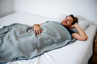 A relaxed adult lying on a bed, wearing a soft weighted blanket that covers the knees and hips, with a gentle, soothing environment and subtle lighting to emphasize comfort and joint relief