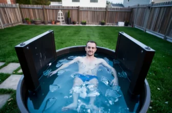 A person standing in a backyard cold plunge tub filled with clear, icy water, surrounded by lush green grass and a wooden fence. The scene is set at dusk with soft, natural lighting that highlights the water's surface and the person's relaxed posture. The background includes a small garden with potted plants and a subtle hint of a modern home in the distance. The overall composition conveys a calm, refreshing, and scientific approach to cold plunging.