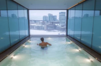 A modern cold plunge pool in a spa setting in Charlotte, NC, with a person stepping into the icy water, surrounded by sleek glass walls and subtle lighting. In the background, a faint view of the Charlotte skyline adds a cityscape touch. The scene conveys a calm, refreshing atmosphere with crisp water and a hint of winter chill.