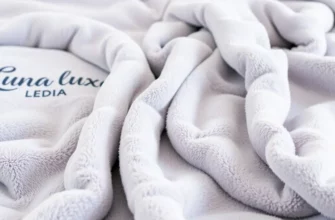 A luxurious, close-up shot of a Luna Luxe weighted blanket draped over a comfortable bed with soft, inviting pillows. The blanket should have a subtle, textured appearance and a calming color palette (e.g., soft grey, lavender, or deep blue). Focus on the plushness and quality of the blanket.