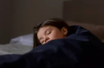A child peacefully sleeping under a weighted blanket in a softly lit bedroom. The room is calming and uncluttered, with muted colors. Focus on the child's relaxed expression and the comforting presence of the blanket.