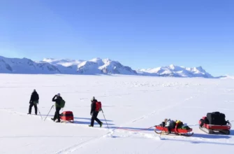 A breathtaking landscape of Antarctica, showcasing the vast icy plains, towering glaciers, and the stark beauty of the polar environment. Include a group of explorers dressed in full cold-weather gear, trekking across the snow with sleds and equipment, capturing the spirit of adventure and resilience. The sky should be clear with a hint of the aurora australis in the distance, adding a touch of natural wonder.