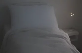 A person comfortably sleeping under a weighted blanket on a bed in a dimly lit bedroom. The blanket should appear soft and plush. Focus on the feeling of relaxation and comfort.