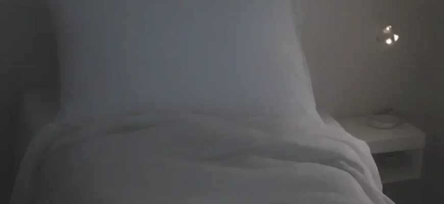 A person comfortably sleeping under a weighted blanket on a bed in a dimly lit bedroom. The blanket should appear soft and plush. Focus on the feeling of relaxation and comfort.