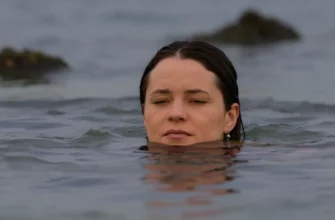 A person emerging from a cold body of water (lake or ocean) with a serene and peaceful expression. The water should be clear and the surrounding environment calm and natural (e.g., a rocky shore, a misty morning). Focus on conveying a sense of tranquility and inner strength.