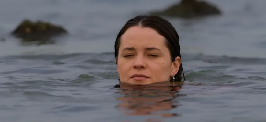 A person emerging from a cold body of water (lake or ocean) with a serene and peaceful expression. The water should be clear and the surrounding environment calm and natural (e.g., a rocky shore, a misty morning). Focus on conveying a sense of tranquility and inner strength.