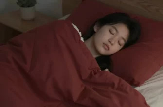 A person sleeping peacefully under a weighted blanket in a dimly lit bedroom. The blanket is a deep red color, and the room has soft, calming colors. Focus on the comfort and tranquility of the scene.