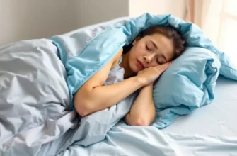 A person sleeping peacefully under a cooling weighted blanket on a bed with light blue sheets. The room is softly lit with natural light coming through a window. Focus on the comfort and relaxation of the scene.