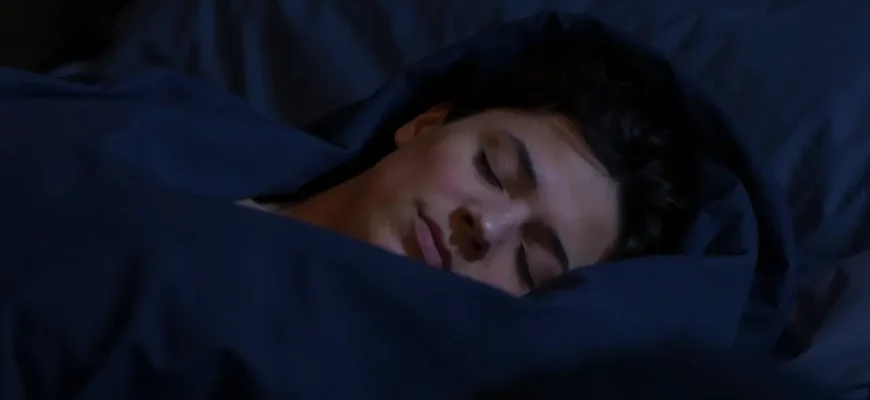 A person sleeping peacefully under a chain weighted blanket in a dimly lit bedroom. The focus is on the blanket's texture and the person's relaxed posture. Soft, diffused lighting creates a calming atmosphere.