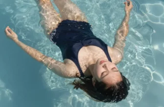A person taking a cold plunge in a clear, outdoor pool on a sunny day. The person is wearing a swimsuit and appears relaxed. The water is crystal clear and reflects the sunlight. Focus on the person's face and body, conveying a sense of well-being and revitalization.