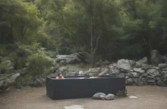 A modern, minimalist outdoor setting featuring a portable cold plunge tub filled with clear, icy water. The tub should be surrounded by lush greenery and natural elements like stones and wood. A person is shown standing near the tub, looking relaxed and refreshed. The scene should convey a sense of tranquility and wellness.