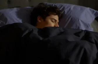 A person sleeping peacefully under a weighted blanket on a bed. The room is dimly lit, suggesting nighttime. Focus on the person's relaxed posture and the blanket's gentle contours.
