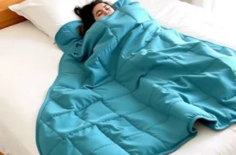 A cozy bedroom scene featuring a neatly made bed with a soft teal weighted blanket draped over it, a person relaxing comfortably under the blanket, and a clean, inviting atmosphere with natural lighting. The focus is on the blanket's texture and color, highlighting its suitability for comfort and sleep.