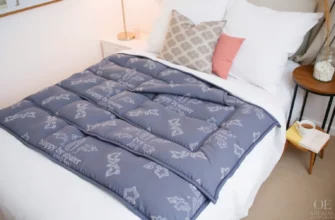 A cozy bedroom scene with a neatly made bed featuring a weighted blanket in a calming color, such as blue or gray. The room should have soft lighting, perhaps from a bedside lamp, and a few decorative pillows on the bed. A small table next to the bed holds a book and a cup of tea, suggesting relaxation and comfort.