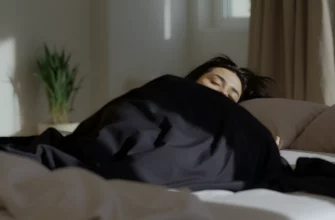 A person lying comfortably on a bed with a weighted blanket draped over them, surrounded by a calm and restful bedroom environment with soft lighting, neutral colors, and minimalistic decor. The scene should evoke relaxation and restorative sleep.