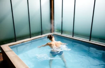 A serene outdoor spa setting with a person gently plunging into a crystal-clear cold water plunge pool, surrounded by frosted glass panels, steam rising from the water, and lush greenery, emphasizing skin revitalization and relaxation