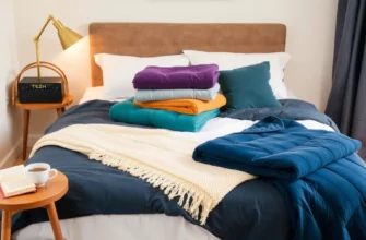 A cozy bedroom scene with a neatly made bed featuring a variety of weighted blankets in different colors and textures. The blankets should be folded and displayed prominently on the bed, with some hanging over the side. The room should have soft lighting and a warm, inviting atmosphere. Include a small table with a cup of tea and a book to suggest relaxation and comfort.