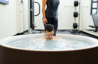 A person standing in a cold plunge tub, with gym equipment in the background, depicting a fitness setting. The person should be in athletic attire, and the scene should convey a sense of preparation or recovery from a workout.