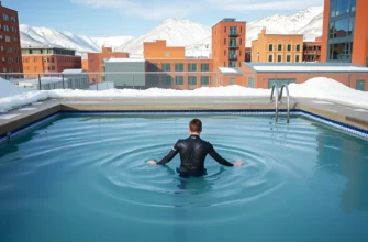 A serene outdoor cold plunge pool in a Denver urban setting, surrounded by snow-capped Rocky Mountains, with a person in a modern wetsuit stepping into the icy water, natural daylight, clean minimalist design, no text or logos