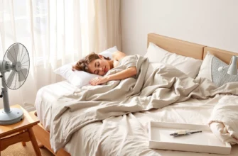 A cozy bedroom scene featuring a person sleeping peacefully under a lightweight, breathable weighted blanket made of cooling materials like bamboo viscose and Tencel, with a fan gently circulating air nearby, soft natural morning light filtering through sheer curtains, and a small tray with a glass of ice water and a lavender sachet on the nightstand — emphasizing summer comfort and thermal regulation