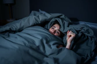 A person lying in bed under a heavy weighted blanket, appearing uncomfortable and anxious, with visible signs of distress such as clenched fists, wide eyes, and shallow breathing, in a dimly lit bedroom at night, soft shadows and muted colors emphasizing the feeling of confinement and unease